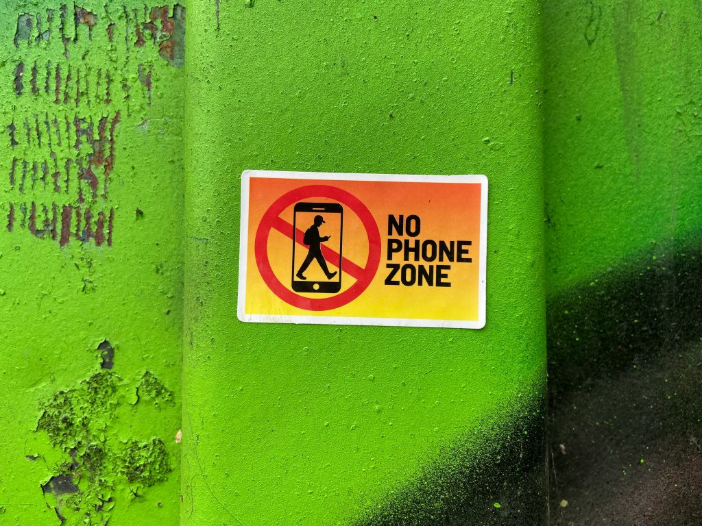 Zettel auf einer grünen Wand mit den Worten: No Phone Zone